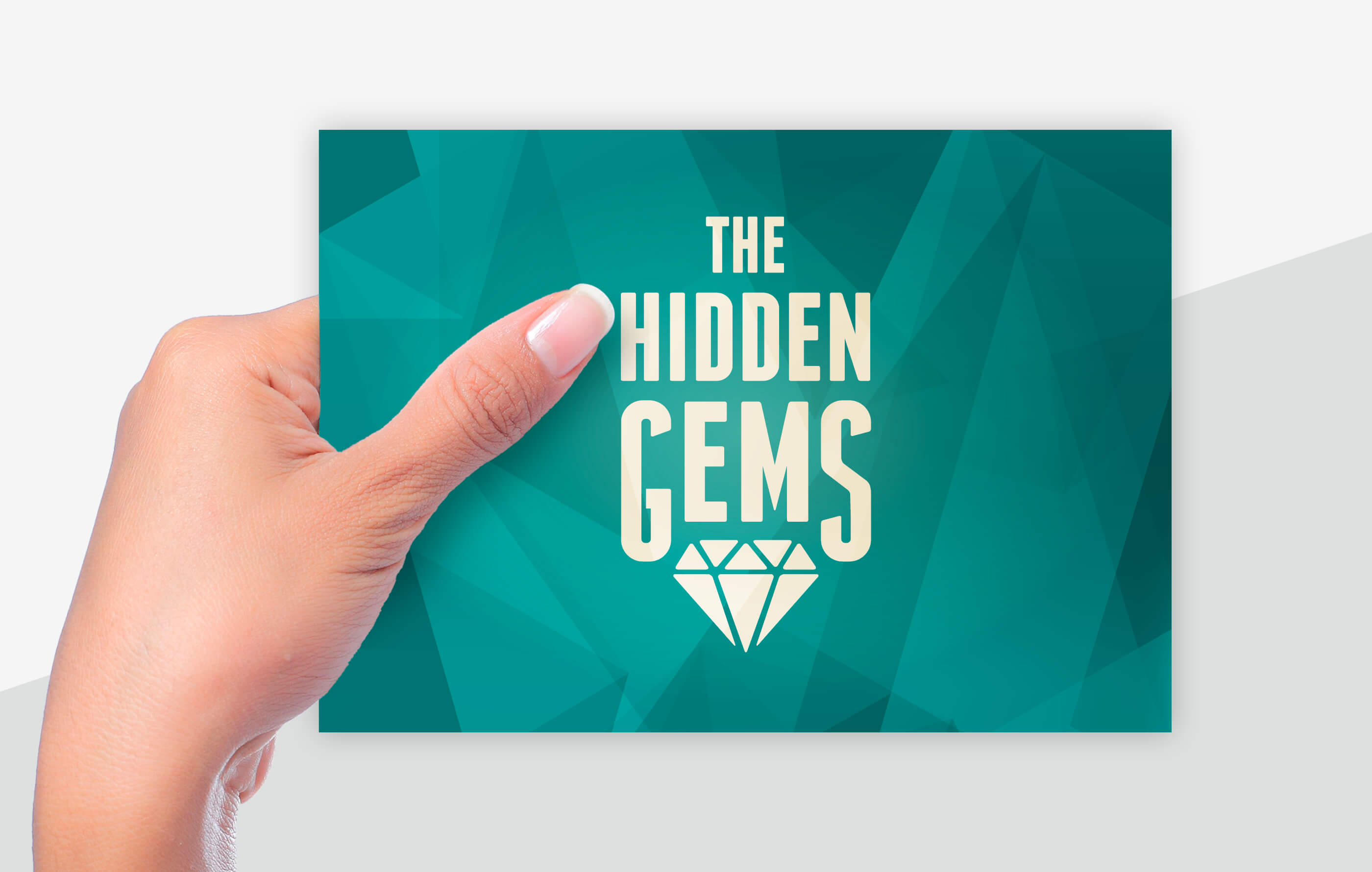 Female hand holding the front side of a Hidden Gems winners card, which features The Hidden Gems logo in light beige on top of a geometric emerald green background