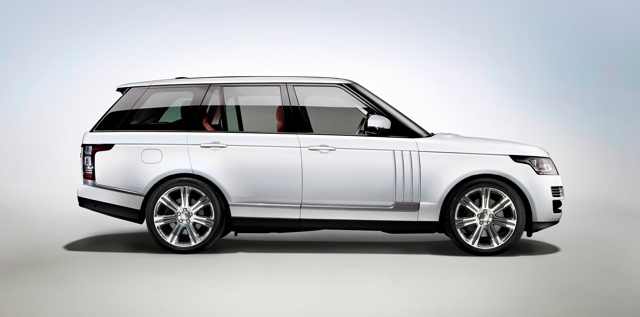 Profile shot of a white Land Rover Range Rover, with red leather interior on a blue and grey background