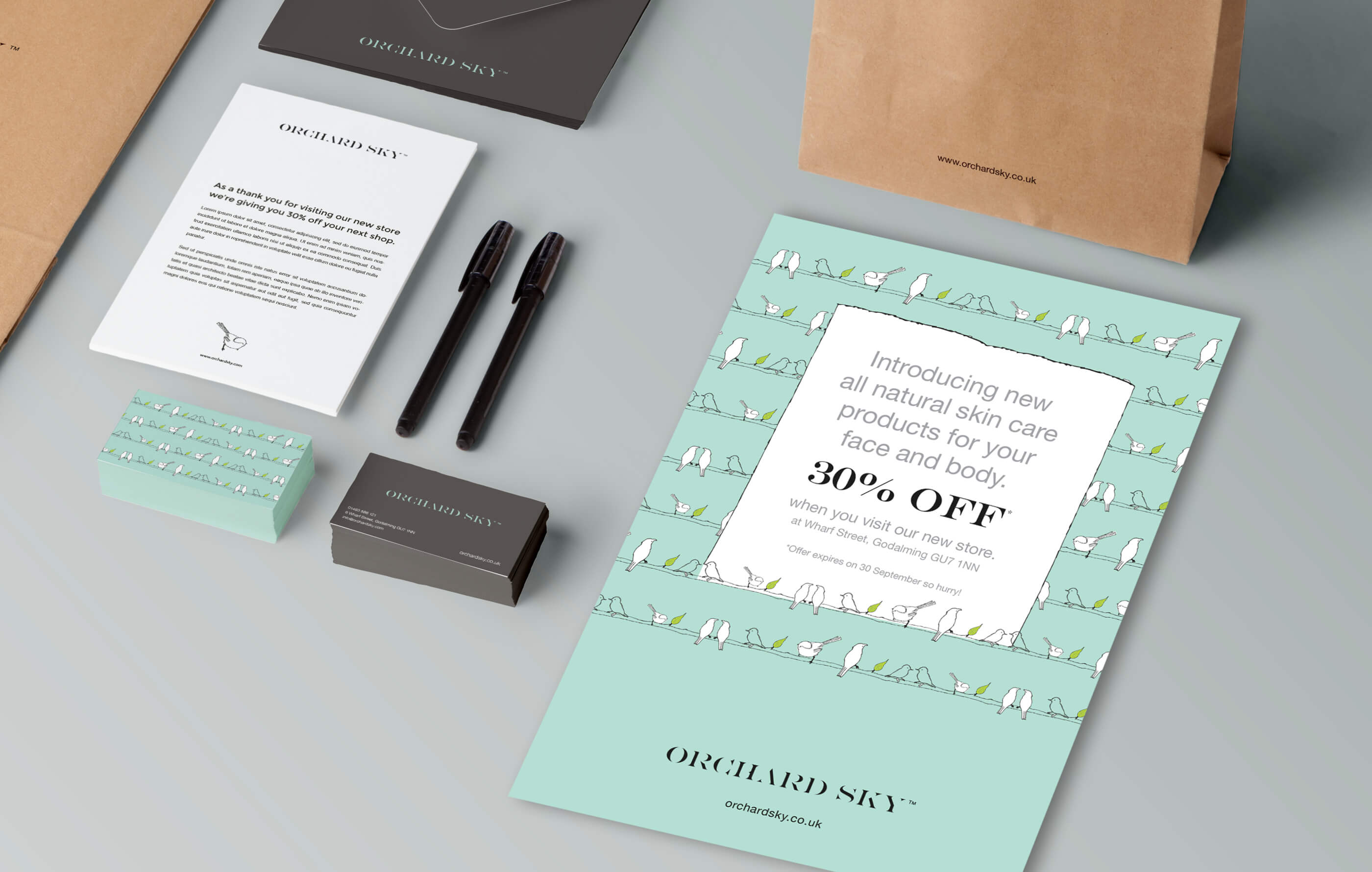 Photorealistic mock up of Orchard Sky stationery and branded collateral, including promo flyer, business card, pen and an envelope