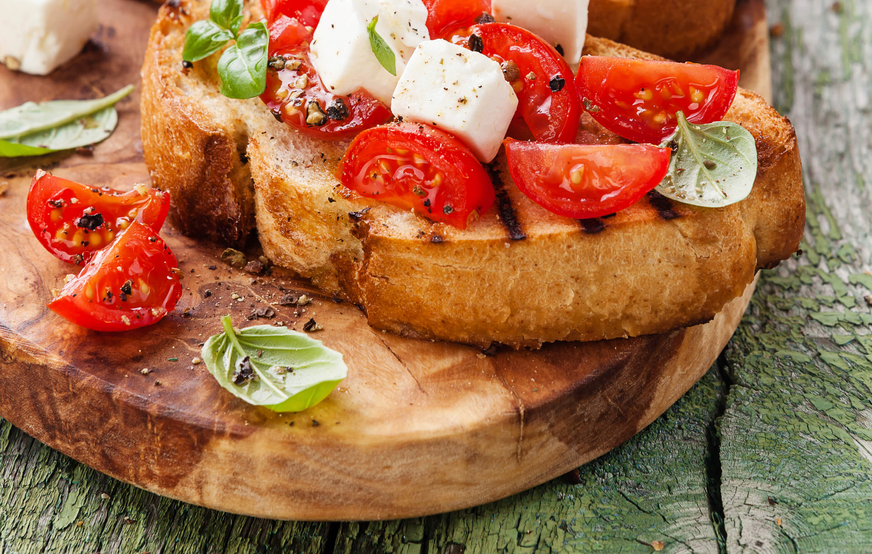 Full spread image of creamy mozzarella, red ripe baby tomatoes and fresh basil on top of rustic bread