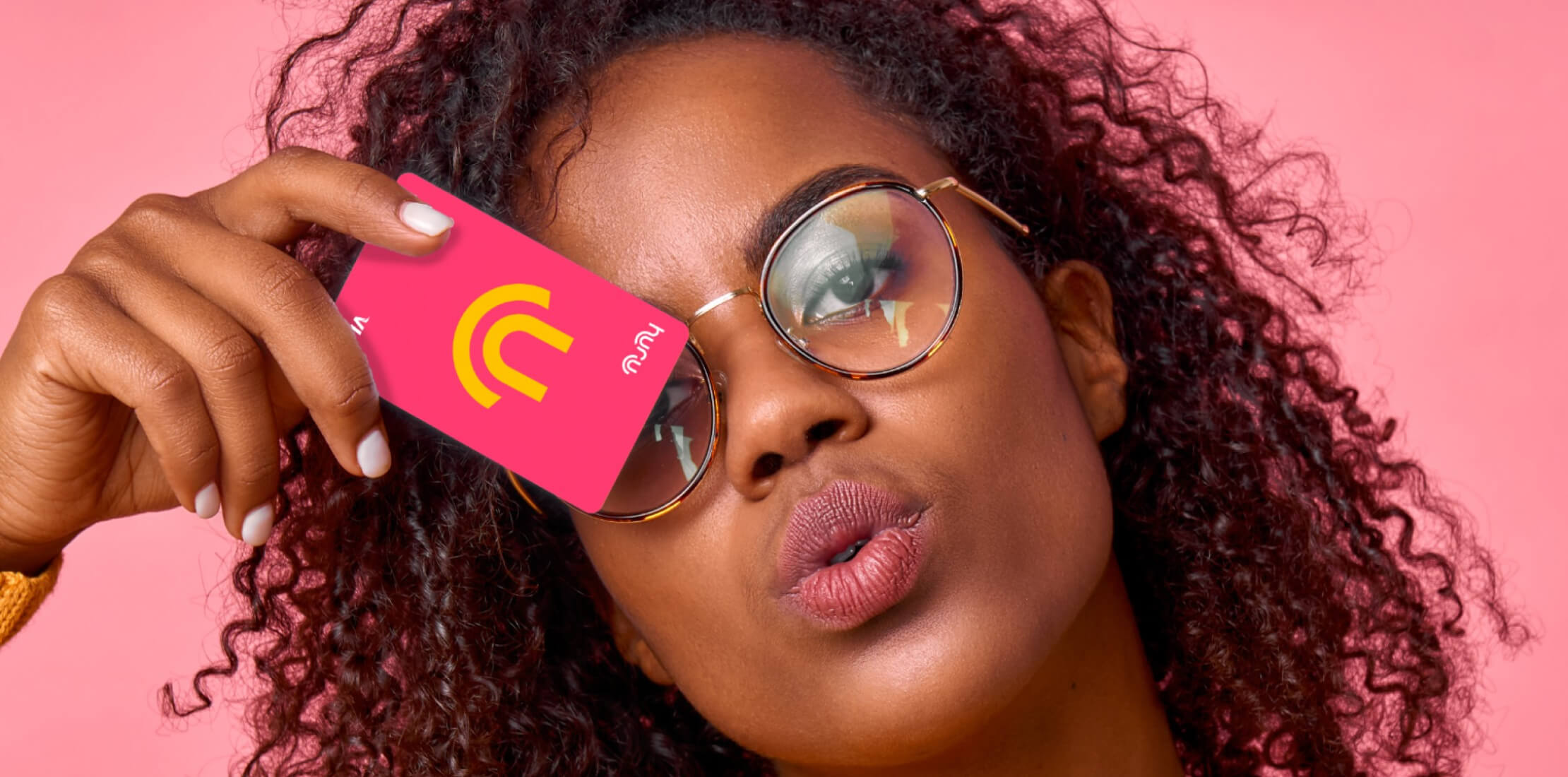 Young black female, wearing glasses, holding a pink Huru-branded bank card up to her face