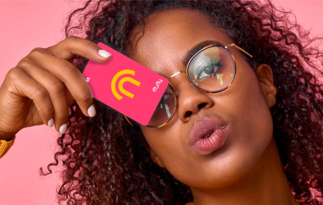 Young black female, wearing glasses, holding a pink Huru-branded bank card up to her face