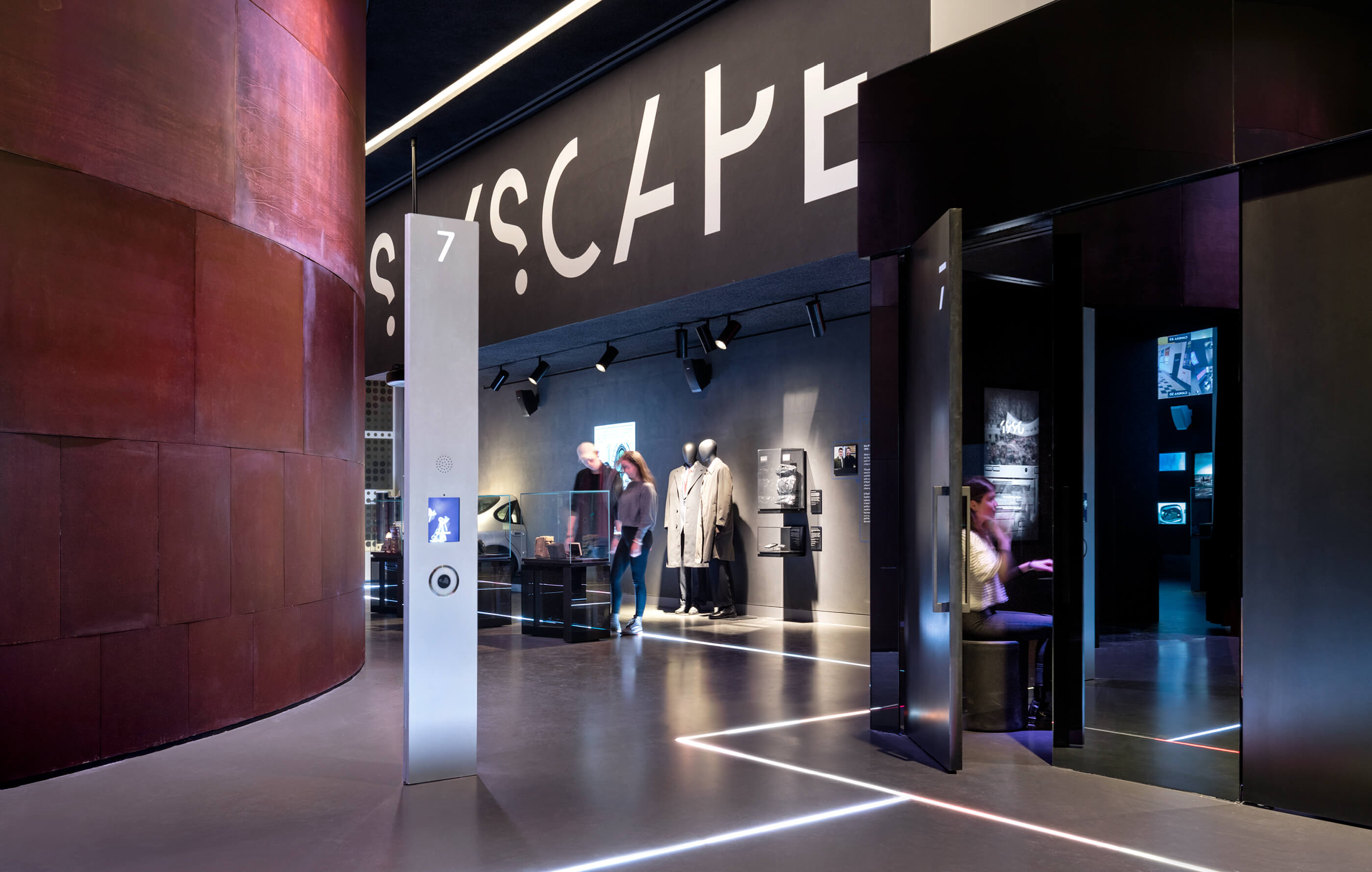 Full screen colour image of the Spyscape museum, designed in cool grey hues with polished concrete floors, black cabinets and white, illuminated walkway strips of light