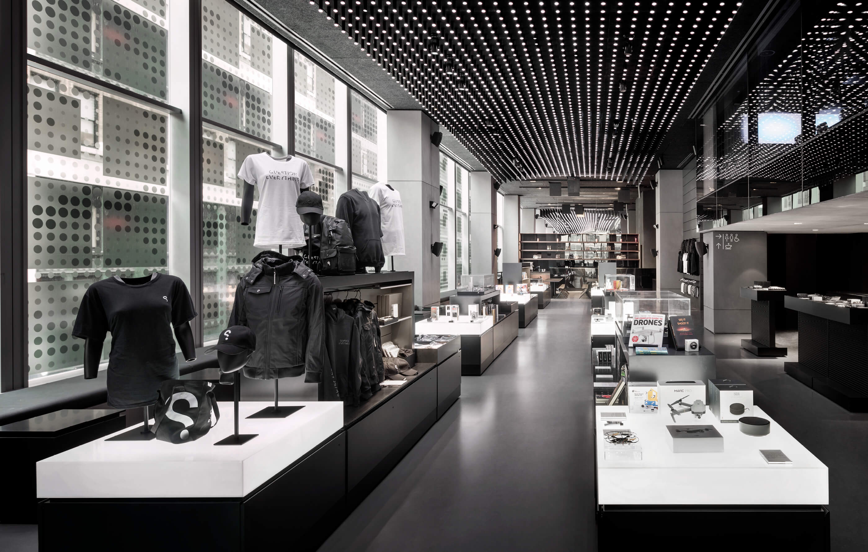 Full screen colour image of the 'Spy Shop' gift shop, designed in cool grey hues with polished concrete floors, black cabinets and white, illuminated display stands
