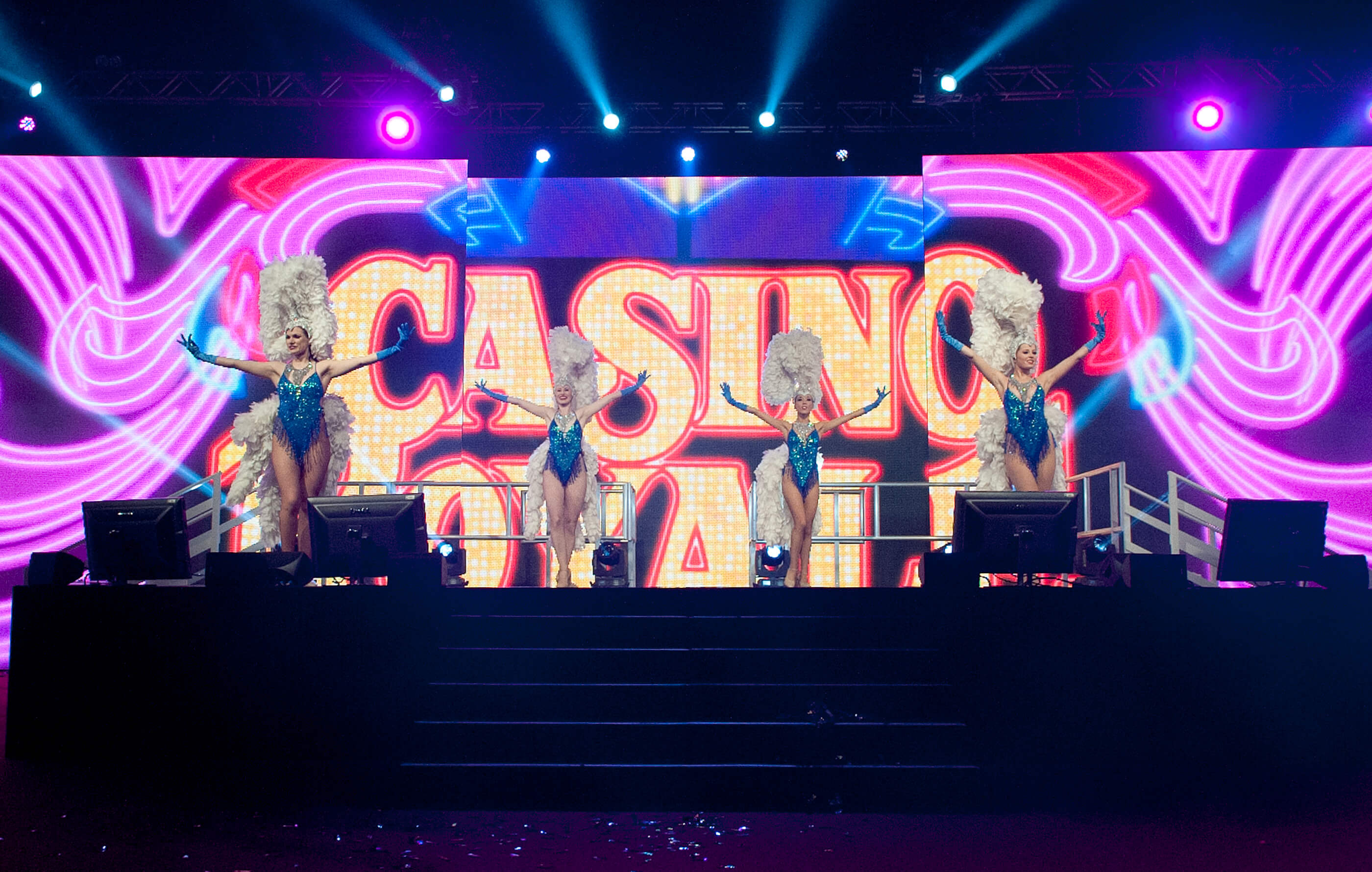 Casino Royale animated stage backdrop, behind four dancers dressed in blue sequin outfits with white feathers
